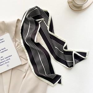 Dettaglio di una sciarpa di seta a righe bianche e nere su un blazer beige con caffè
