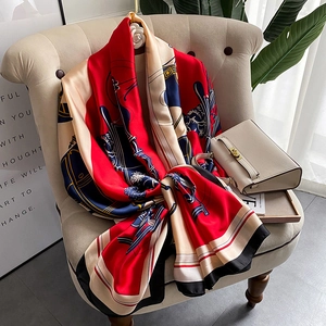 Elegant red silk scarf with equestrian horse carriage print on a beige sofa
