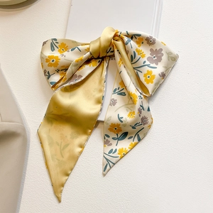 Détail d'un foulard en soie noué en nœud avec des imprimés floraux jaunes sur satin
