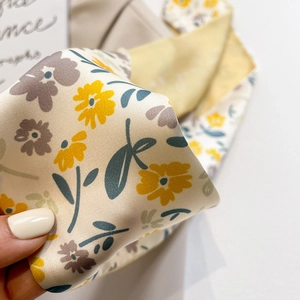 Détail macro du tissu satiné d'un foulard aux fleurs jaunes et texture soyeuse fine