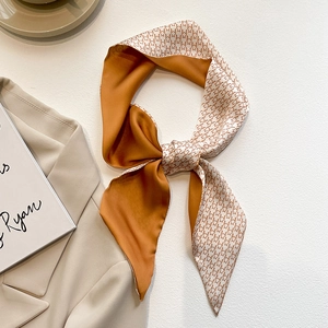 Détail d'un foulard en soie pied-de-poule caramel noué en nœud sur un blazer beige