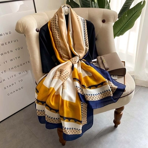 Elegant yellow silk satin scarf with geometric pattern draped on a classic beige chair