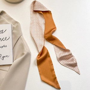 Détail d'un foulard twilly en satin orange caramel avec motif pied-de-poule et étoiles
