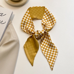 Détail d'un foulard étroit à damier jaune et blanc noué sur un blazer beige