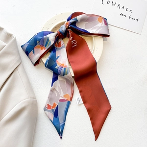 Detail view of floral satin skinny scarf tied in a bow on a white ceramic tray