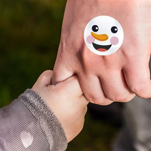 Close-up of a round cartoon snowman sticker applied to a hand for holiday decoration