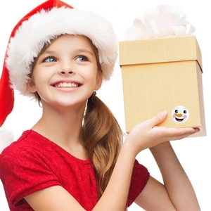 Smiling girl holding a gift box decorated with a cute Christmas snowman face sticker