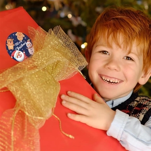 Detail of a Christmas sticker on a red gift box held by a child near a Christmas tree