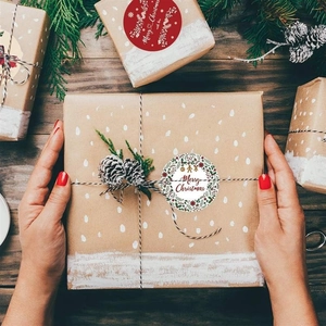Close-up of Merry Christmas snowflake stickers applied to a kraft gift box on wood