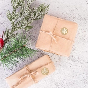 Détail d'autocollants de Noël dorés avec flocons blancs sur boîtes cadeaux en kraft