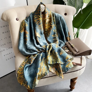 Elegant silk-like shawl with golden floral prints on a muted blue background draped over a chair
