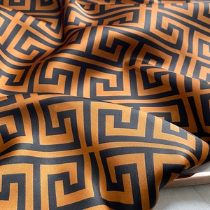 Macro detail of silk-like beach shawl featuring golden Greek key patterns and smooth texture