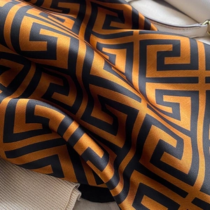 Macro shot of silk scarf with orange Greek key patterns and luxurious satin texture
