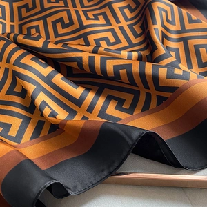 Detail of silk scarf showing orange and black geometric pattern and glossy satin texture