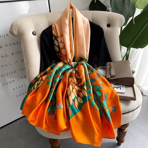 Floral silk-like scarf with orange and green leaf patterns draped over a mannequin