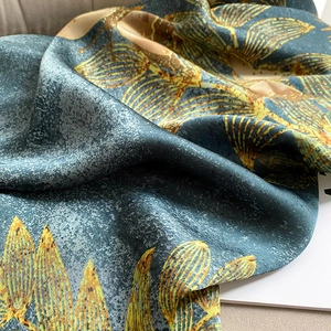 Detail of silk-like beach shawl featuring golden leaf prints on deep blue fabric texture