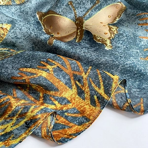Detailed view of silk scarf with golden butterflies and coral patterns on grey-blue satin