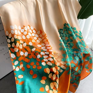Close-up of champagne silk scarf with artistic leaf patterns and pearl-like luster finish