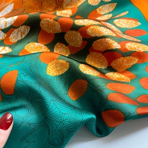 Macro detail of silk scarf showing emerald green fabric with orange leaf patterns