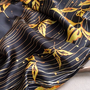 Close-up of black silk scarf featuring golden leaf patterns and fine striped textures