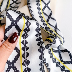 Macro detail of twilly silk scarf featuring black diamond chain patterns and yellow lines