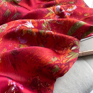 Macro detail of red floral silk scarf showing glossy satin texture and artistic oil painting patterns