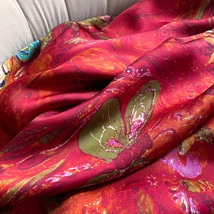 Detailed close-up of vibrant red floral silk-like scarf with artistic butterfly prints