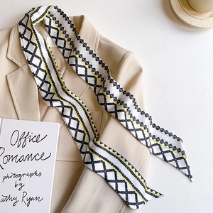 Detail of printed twilly scarf on beige suit with geometric diamond pattern and yellow lines