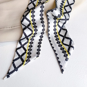 Macro detail of silk scarf featuring black geometric chain print and yellow stripes