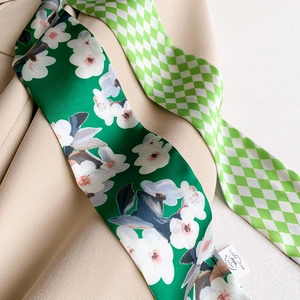 Detail of green checkerboard and floral satin skinny scarf tied on a chic beige blazer