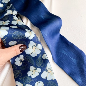 Detail of silk scarf showing white floral patterns and gold leaf outlines on navy blue satin