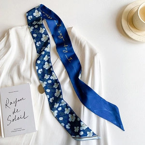 Detail of a floral navy silk twilly scarf styled on white shirt with lifestyle props