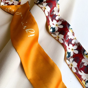 Macro detail of mustard yellow satin headband with text and tropical floral print scarf