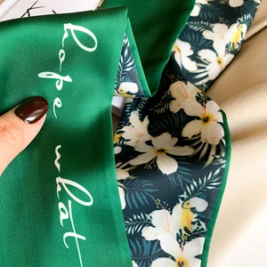 Close-up of a double-sided silk scarf with green satin surface and tropical floral prints