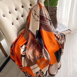 Elegant large silk scarf with orange and brown chain print draped on a beige chair