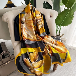 Elegant floral silk shawl with yellow and black patterns draped on a beige sofa