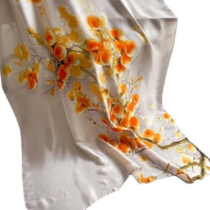 Elegant cream silk scarf with vibrant orange floral patterns in graceful drape style