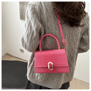 Detail of rose pink crocodile pattern handbag worn as a cross-body on a grey sweater