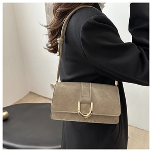 Gros plan du sac porté épaule en cuir taupe mat avec boucle dorée en U sur un mannequin