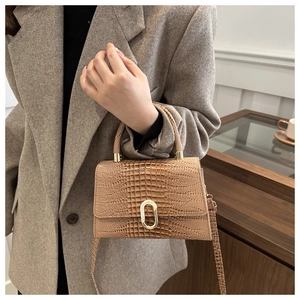 Detail of crocodile embossed leather texture and gold oval lock on a brown handbag