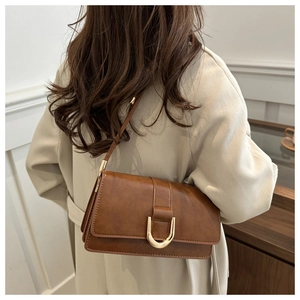 Detail of caramel brown PU leather bag with gold horseshoe buckle and long shoulder strap