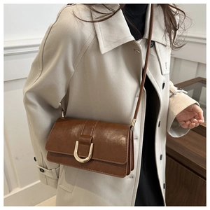 Détail d'un sac à bandoulière en cuir marron avec boucle décorative en fer à cheval dorée