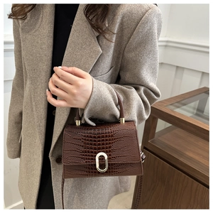 Detail of dark brown croc-embossed handbag with elegant metallic oval twist lock closure