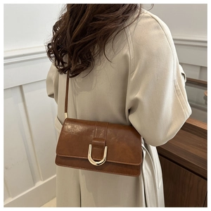 Détail d'un sac bandoulière en cuir marron avec boucle en U dorée sur un manteau beige