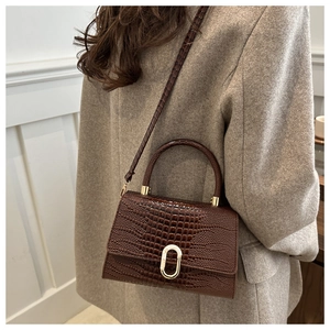 Detail of dark brown faux leather handbag with crocodile texture and gold oval buckle