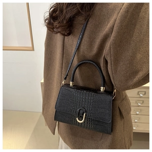 Detail of black crocodile texture bag with gold U-shaped lock on a brown wool coat