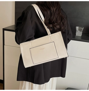Detail of minimalist cream leather tote bag featuring front pocket and elegant letter print