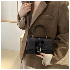 Detail of black crocodile embossed kelly bag with golden metal twist lock on tweed blazer