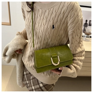 Détail d'un sac bandoulière vintage en cuir vert avec boucle en U dorée sur un mannequin