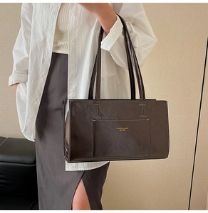 Detail of dark brown glossy leather tote with contrast stitching and golden logo